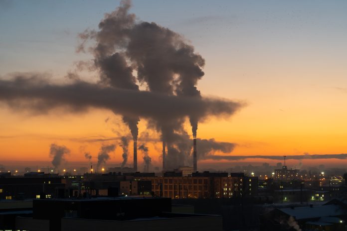 Air pollution and global warming. Smoking chimneys of thermal power plant at sunset in winter city Chemical factory chimneys with raising smoke against red sunset sky in winter city during strong frost. View from afar of thermal power plant pipes emitting hazardous toxic pollutants into atmosphere