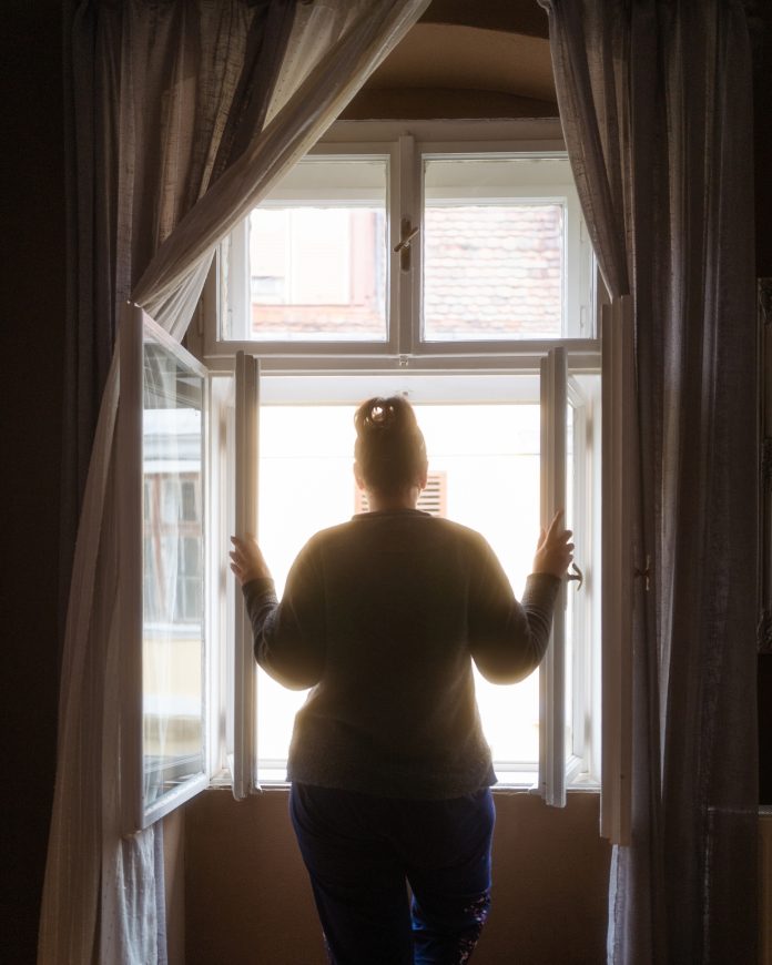 woman looking out window of accommodation - domestic abuse victims