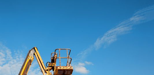 Telescopic boom lift rised up on blue sky background delivered to constraction site ready to be used by steel frame erectors, roofers and painters, representing the Hinkley Point C unrest