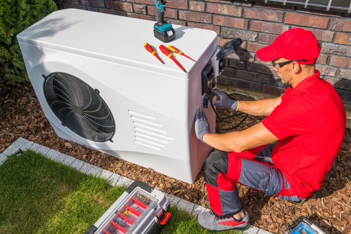 Professional Middle Aged HVAC Technician in Red Uniform Repairing Modern Heat Pump Unit. House Heating and Cooling System Theme, representing the Boiler Upgrade Scheme