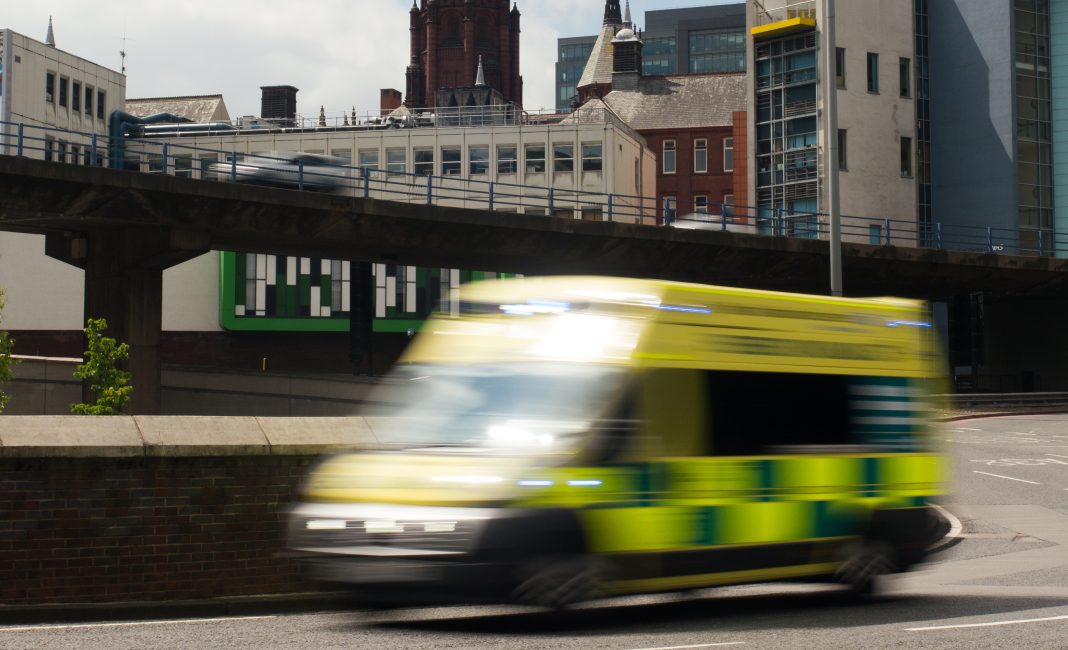 Motion-blurred ambulance travelling at speed on city roads. In the background is Birmingham's Children's hospital, representing the Birmingham hospital upgrades