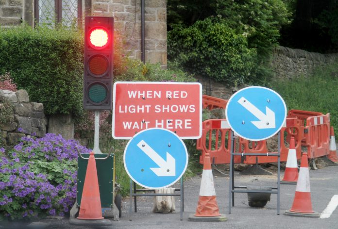 Roadworks with temporary traffic lights in rural village, representing the cancelled northern ireland road schemes