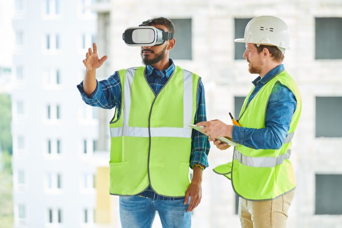 Waist up portrait of two modern construction workers using VR gear to visualize projects on site, representing construction technology trends