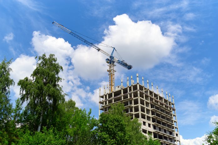 Construction site, building and trees, crane, blue sky, representing the biodiversity net gain deadline