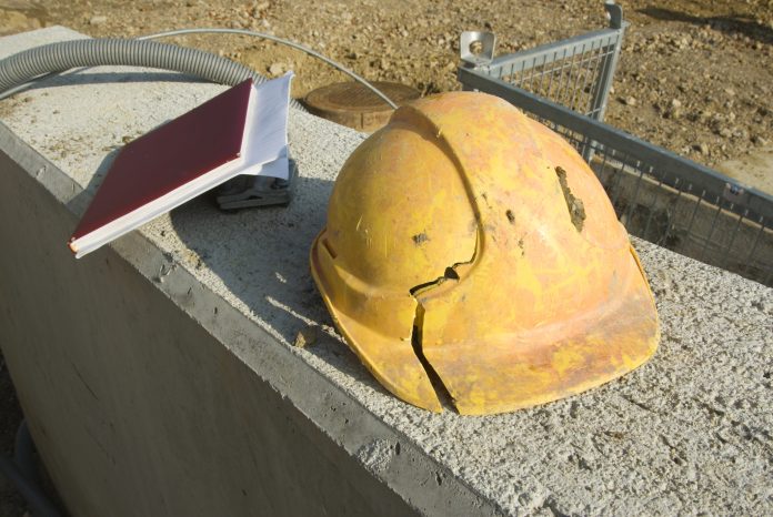 Beschädigter Bauhelm nach einem Arbeitsunfall gemeinsam mit Protokollbuch