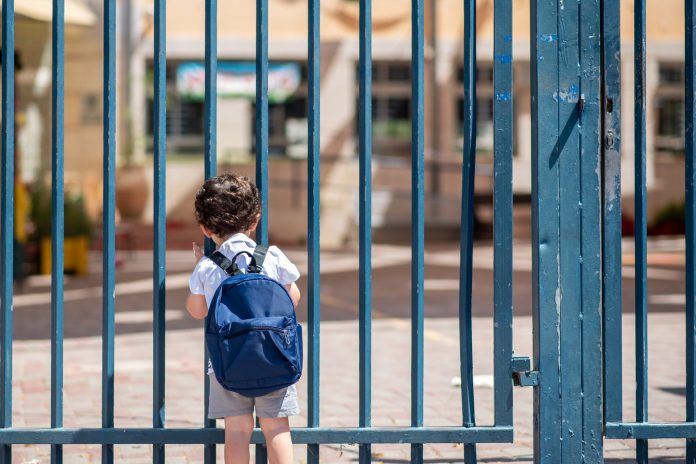 Industry reacts to RAAC panels in UK schools scandal Kid with school backpack look on schoolyard towards an open entrance or exit door. Representing schools closed due to structural risk of RAAC panels