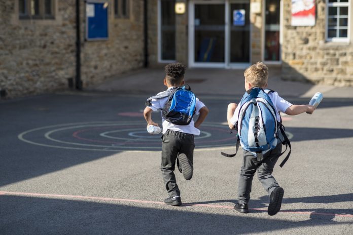 Rear view of two boys running in their school yard in the North East of England. They are running towards the door with their backpacks on. Representing the new net zero school