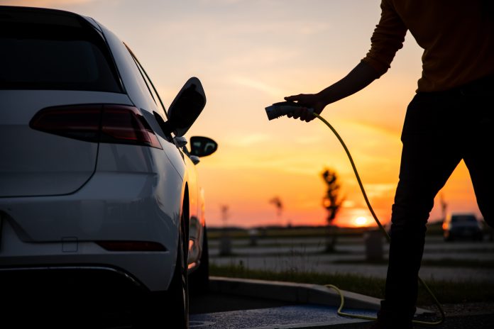 Silhouette of man inserting plug into the electric car charging socket Silhouette of african american man plugging an EV plug into his car for charging at station