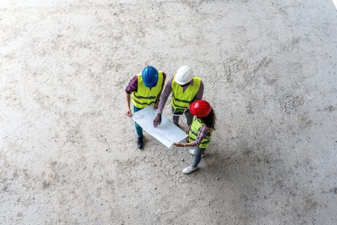 Team of construction workers discusses the details of the project with the executive supervisor using tablet and blueprint