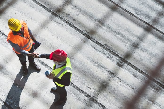 Enhance your safety & efficiency with cloud-based defect management tool Over the head aerial view of a senior man architect and African American engineer shaking hands on construction site.