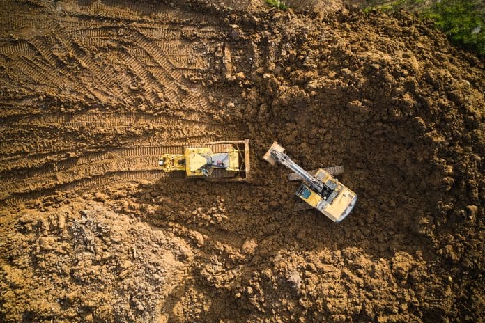 Electrifying industry: The road to diesel-free construction sites Bulldozer is scraping a layer of soil and excavator is digging and dumping dirt, representing diesel-free construction sites