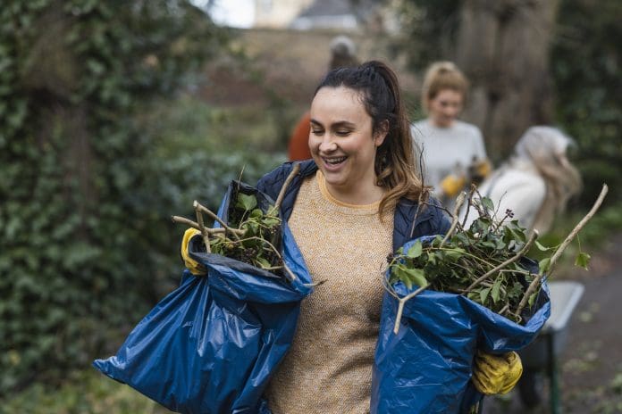 Making a pact on social impact A front view of a young brunette woman carrying two bags of garden waste that is to be composted and reused. She is working on a community space garden in Hexham in the North East of England with a group of friends.