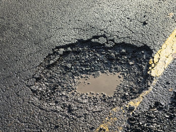 Close-up of the effects of road weathering and neglect - a deep pot hole causing a danger to drivers. Image represents redirected pothole funding