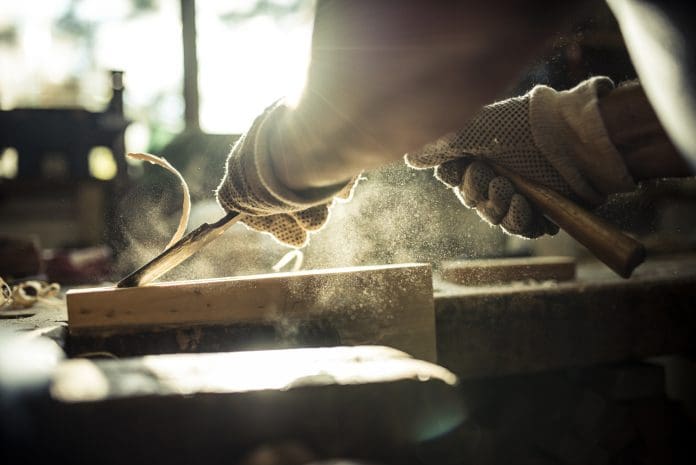 A caucasian senior adult carving wood in a workshop, representing the skills recognised in the BWF Awards