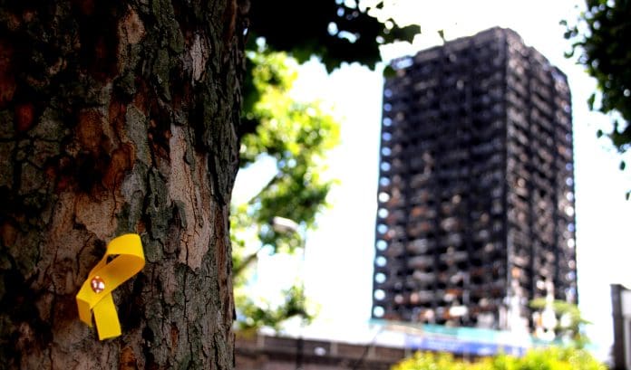 Failure to address building safety risks could cause ‘Grenfell-scale tragedy’, warns ex-civil servant Grenfell tower in the background with a Yellow Ribbon commemorating those lost pinned to a tree