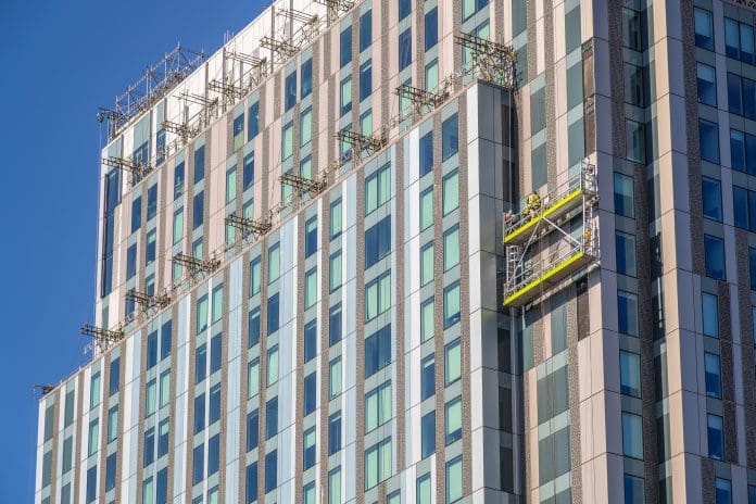 Unidentified construction workers on suspended scaffolding inspecting / installing cladding on a high rise building in London Unidentified construction workers on suspended scaffolding inspecting / installing cladding on a high rise building in London, England, UK