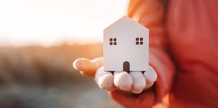 Hands holding wooden house against sunset light for sale or rent. Property investment and house mortgage financial real estate
