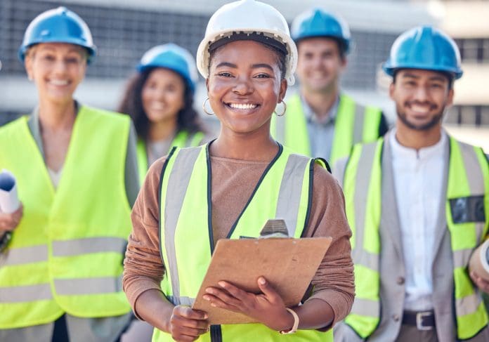 female construction worker standing on a building site with her colleagues in the background stock photo, representing the construction skills shortage