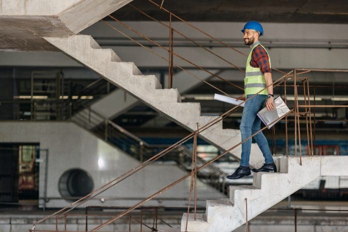 Young professional engineer worker in protective helmet and blueprints paper on hand at the house building construction site