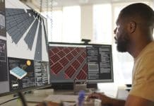Good construction data practice is critical to efficiency Close up stock image of an African American man working at a computer screen. He’s working on CAD software looking at the design of a solar panel array in CAD with data, representing construction data