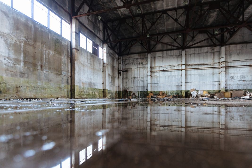 Inside of flooded dirty abandoned ruined industrial building with water reflection, representing need for parametric flood insurance