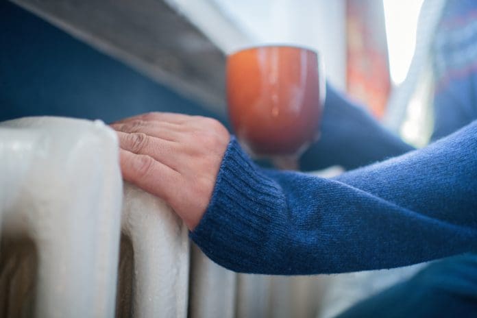 Man in warm sweater with hot tea near radiator in winter, representing heating system flushing