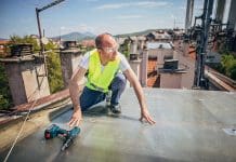 What are the four pillars of a watertight flat roof? One mature man, roofer, installing a new flat roof on residential home.
