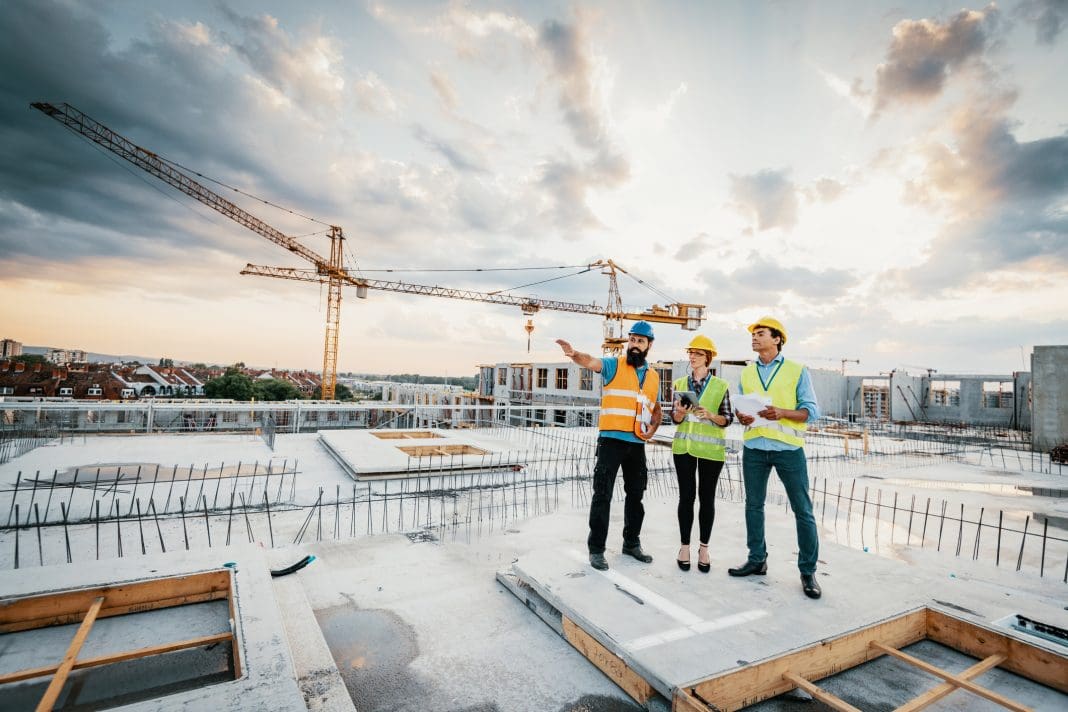 Employees working on construction site, wearing protective equipment and discussing next construction phase - full length models visible on the image