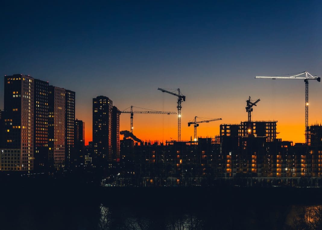 Metropolitan skyline with tower cranes building high-rise residential buildings in evening time. Steel frame structure in sunlight. Industrial background. Lifestyle