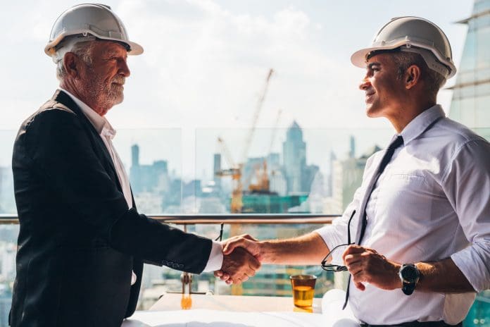 Two engineer wear safety helmet shaking hands after meeting for architectural project working with partner. Worker and customer having agreement in factory. Industry, Engineering, construction concept.