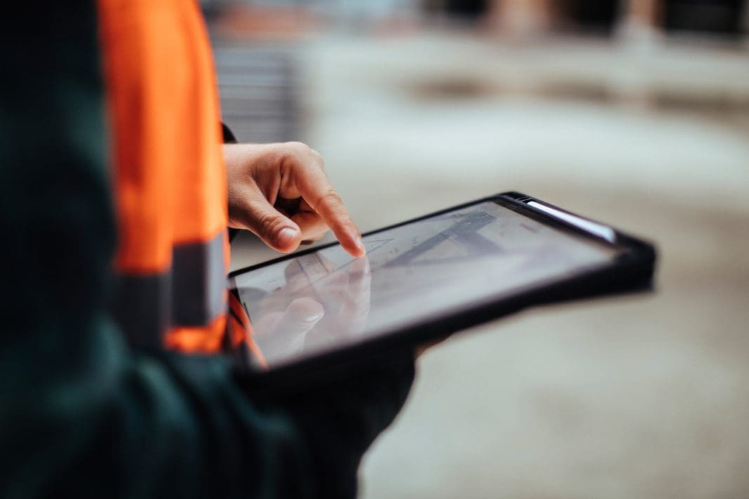 Unrecognizable construction worker hands holding a digital tablet while working outdoors, representing bim models