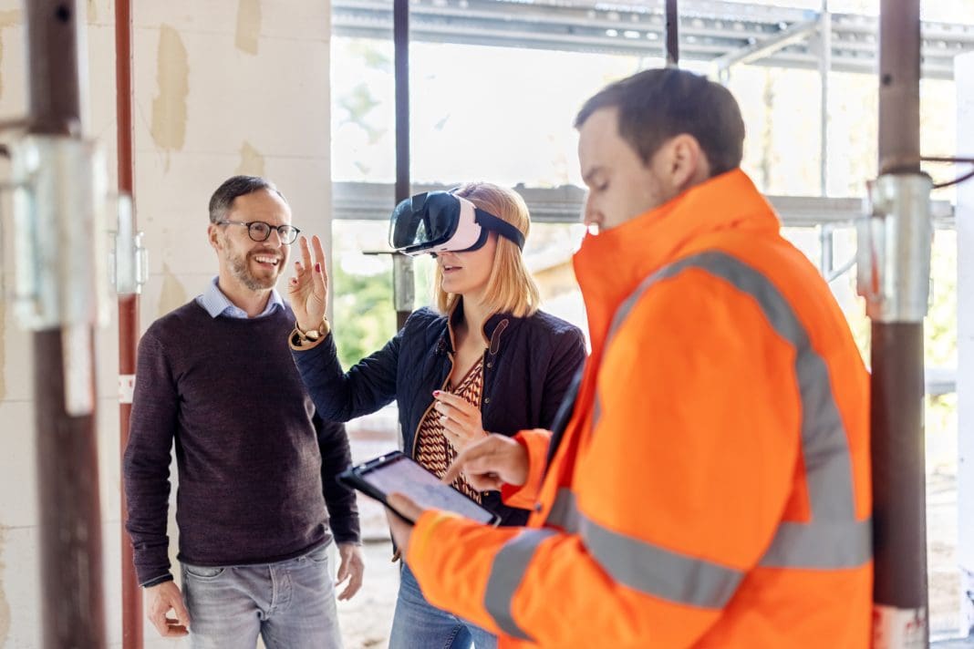 Building contractor showing home renovation design to a couple using virtual reality glasses at construction site. Woman wearing virtual reality headset discussing home renovation project with an architect using digital tablet.
