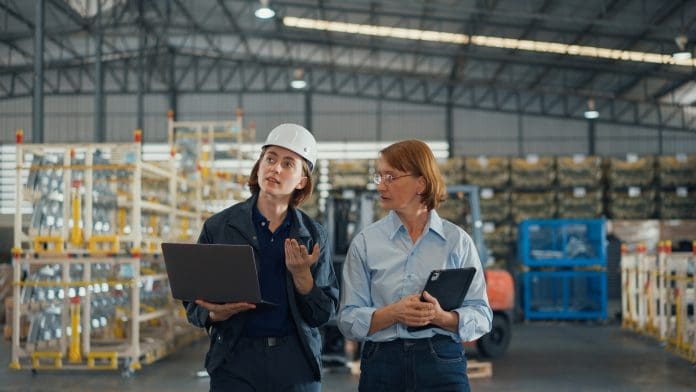 Young caucasian woman worker and mature female manager walking checks stock inventory with tablet and laptop and discuss talk together in retail warehouse. Logistic industry business. Young caucasian woman worker and mature female manager walking checks stock inventory with tablet and laptop and discuss talk together in retail warehouse. Logistic industry business concept.