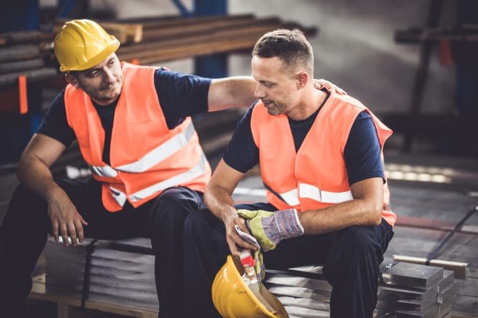 Sad manual worker being consoled by his colleague in aluminum mill.