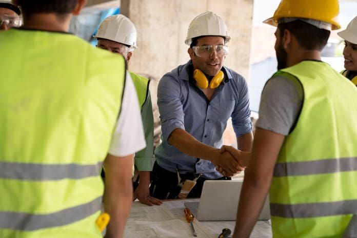 Latin american architect welcoming new partner at a construction site handshaking very cheerfully