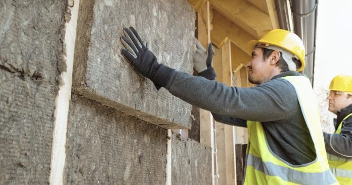 Addressing common issues in procuring sustainable materials for construction projects Construction workers placing eco insulation blocks into the frame on the outer wall of the house.