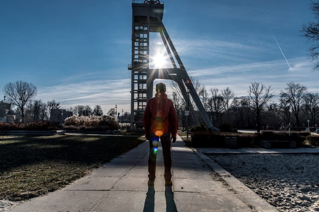 A man in a red winter anorak watching the sunrays through the structure of a mine shaft in the Silesia landscape representing aeco collaboration