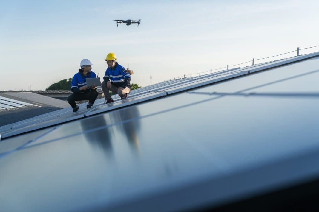 Specialist technician professional engineercontrol drone checking top view of installing solar roof panel on the factory rooftop under sunlight. Engineers holding tablet check solar roof, representing AI in construction