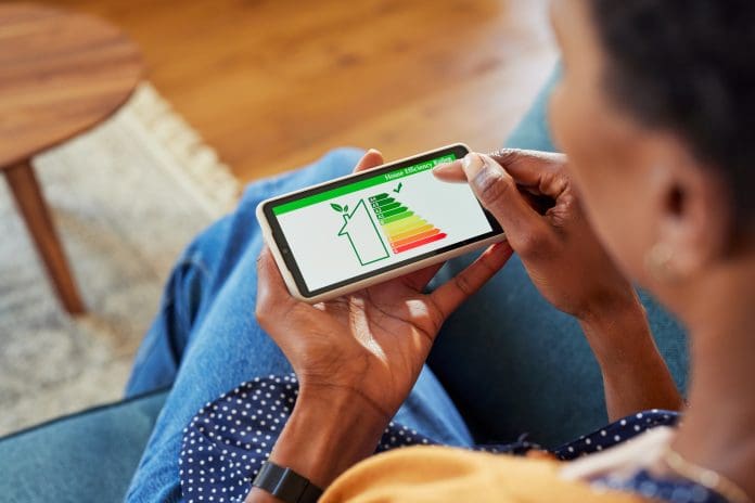 Close up of african american woman holding smartphone with energy efficiency chart and class on screen. Black female hands holding smart phone and looking at house efficiency rating. Concept of ecological, eco renovation and bio energetic house.