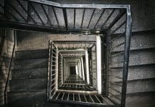 Government halts construction of 38,000 homes over second staircase delay A view from the top, looking down into an industrial building stairwell. Metal stairs and railings lead down several floors into the basement, representing the legal situation of a second staircase