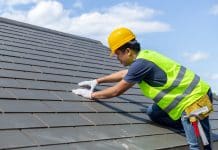 Roofing contractors survey: Rising demand, late payments and sustainability in procurement Roof repair, worker with white gloves replacing gray tiles or shingles on house with blue sky as background and copy space, Roofing - construction worker standing on a roof covering it with tiles.