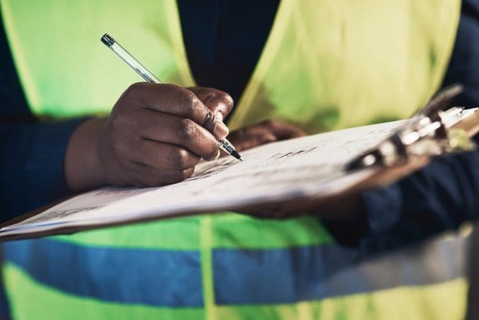Cropped shot of an unrecognizable contractor standing alone in the warehouse and writing on a document during stock-take Signing off the shipment