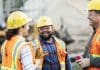 Bouygues UK boosts efficiency, visibility and risk management with payment applications A group of three multi-ethnic workers at a construction site wearing hard hats, safety glasses and reflective clothing, smiling and conversing. The main focus is on the mixed race African-American and Pacific Islander man in the middle. The other two construction workers, including the woman, are Hispanic.