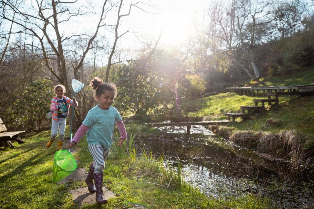 A shot of two young sisters running outdoors near a pond in Hexham, Northumberland. They are holding butterfly fishing nets, to catch animals from the Pond.
