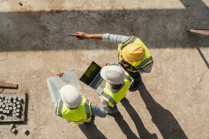 Top view, Team engineer building inspection use tablet computer and blueprint working at construction site. Civil Engineer, Contractor and Architect discussing in construction site, representing a culture of safety in construction