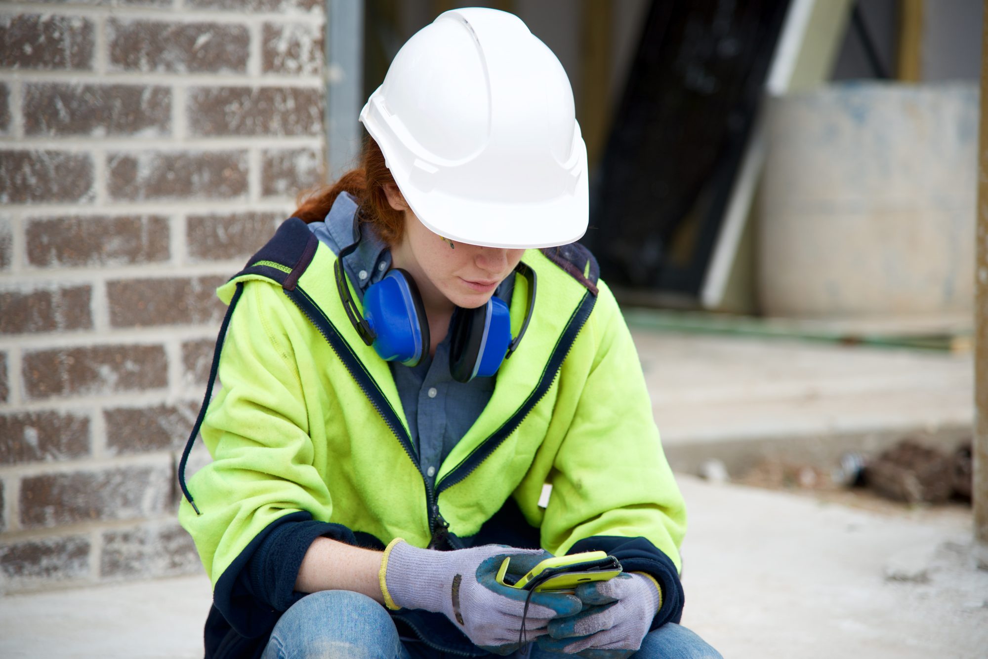 View of a female construction worker taking a break, having a cuppa and using smart phone