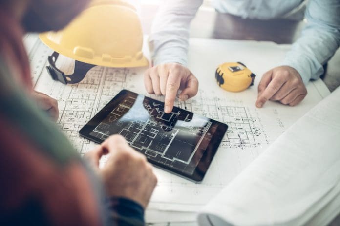 Hands of an architect and a building contractor pointing at the architectural plan on a tablet computer. They have a coordination meeting to solve the site problems.