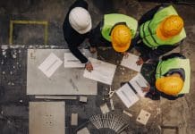 What contractors and developers need to know about the JCT Design and Build Contract and party wall proceedings Workers and manager in safety helmets working with documents at factory