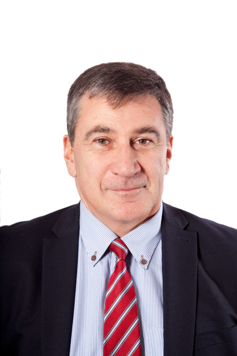 Headshot of Kenny Ingram facing the camera against a white background wearing a dark suit jacket, light shirt and tie