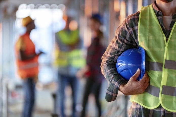 Man holding blue helmet close up Man holding blue helmet close up. Construction man worker with office and people in background. Close up of a construction worker's hand holding working helmet.